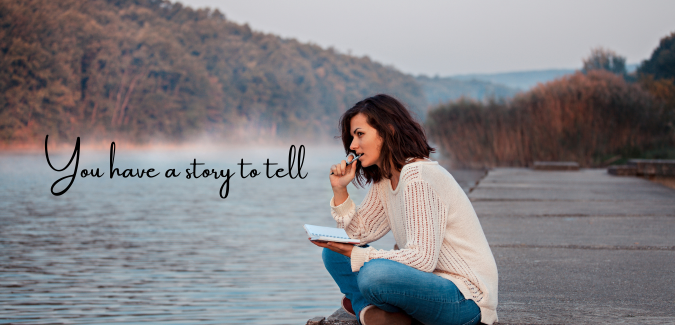 Woman sitting by the water writing in a journal, the words "You have a story to tell" are on her left